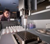 A researcher watches a robot load a tray with samples.