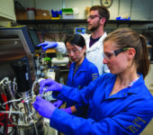 Three scientists in a laboratory prepare an instrument for use.