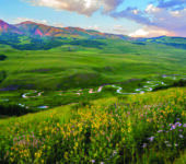 Meadow with mountains above a river.