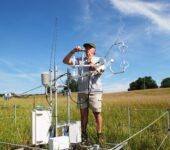 A researcher sets up an instrument tower in an open field.